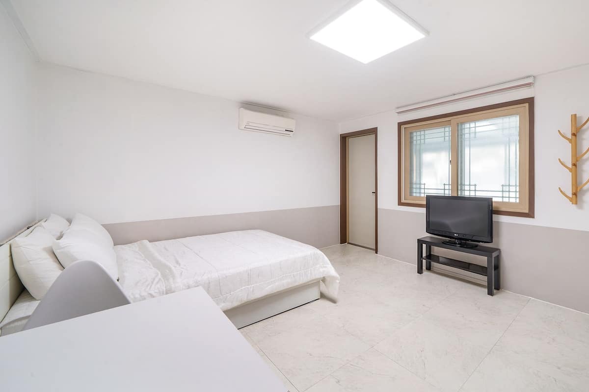 A bedroom with a bed, a TV on a stand, a coat rack, and a door.
