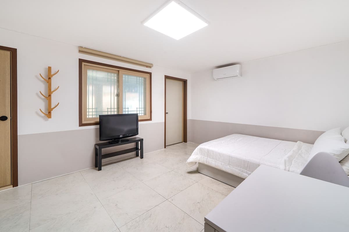 A bedroom with a bed, a TV on a stand, a coat rack, and a window.
