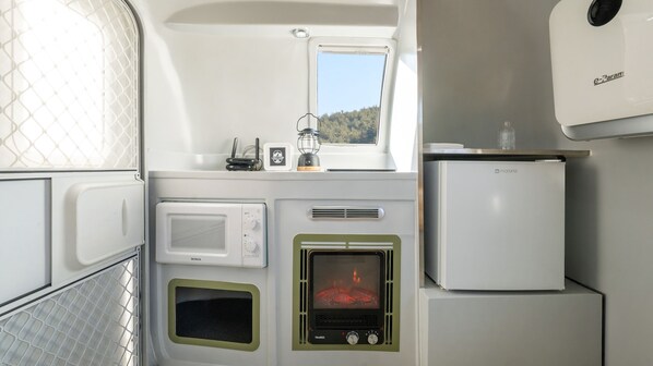 A compact kitchenette with a microwave, a stove with a visible flame, a refrigerator, and a window providing a view of the outdoors. - Yangyang Lira Camp (Yangyang)