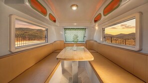 A train carriage interior with a central table, seating on both sides, and windows with views of a desert landscape. - Yangyang Lira Camp (Yangyang)