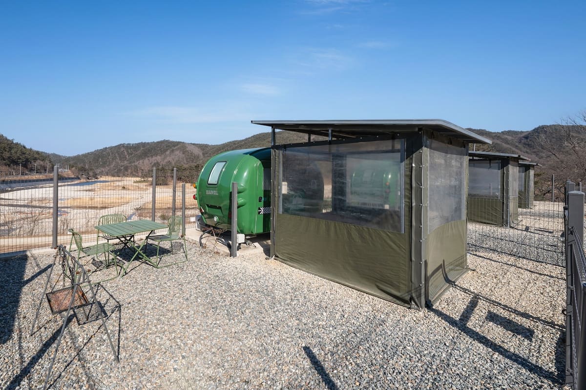 Una cocina al aire libre portátil con una parrilla verde, una mesa con sillas y un refugio cubierto.