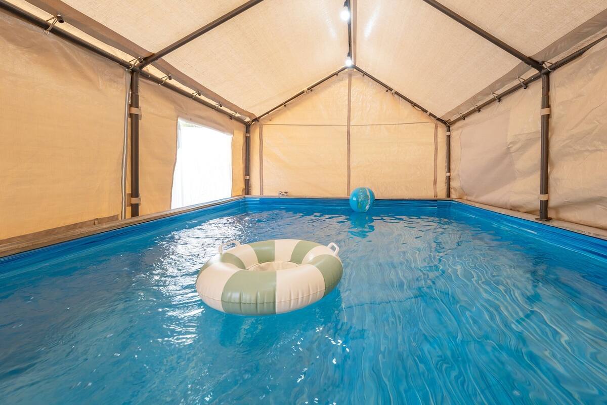 An indoor swimming pool with a clear water surface, a pool float, and a tent-like structure overhead.