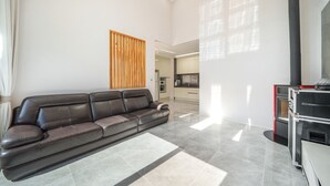 A modern living room with a leather sofa, a wooden slat wall, a kitchen area, and a fireplace. - Daebudo Freesia Private Pool Villa (Ansan)