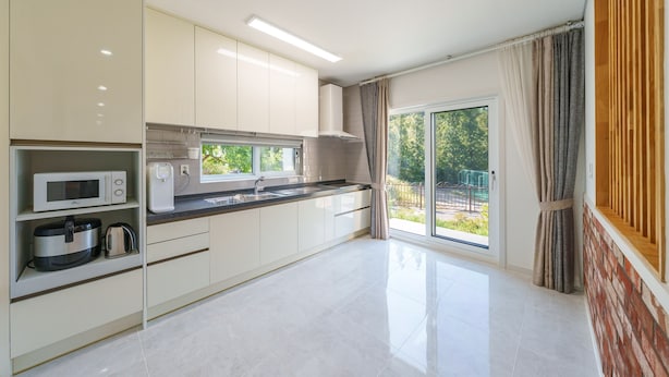 A modern kitchen with white cabinets, a microwave, a kettle, and a large window. - Daebudo Freesia Private Pool Villa (Ansan)