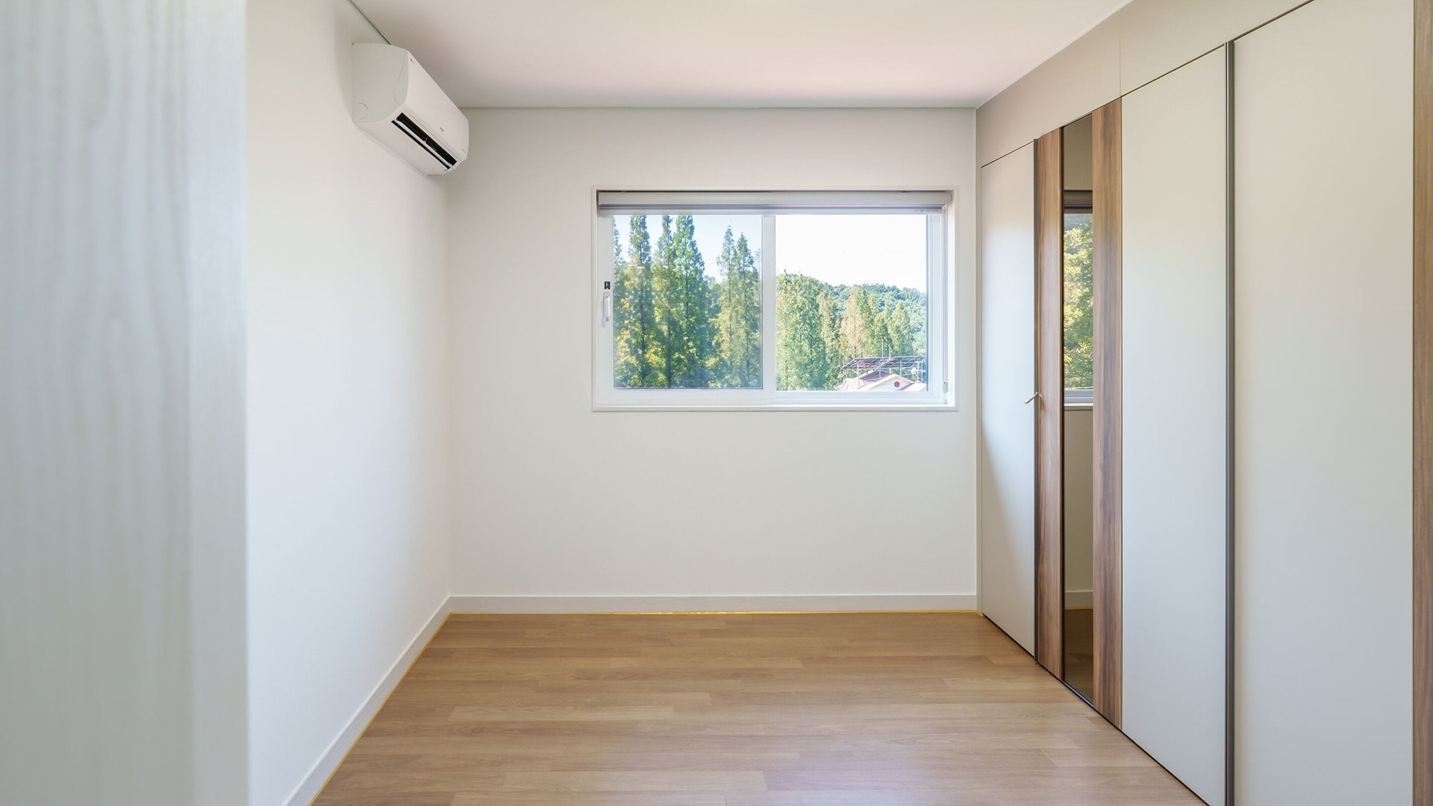 A room with a large window, wooden flooring, and a sliding door.