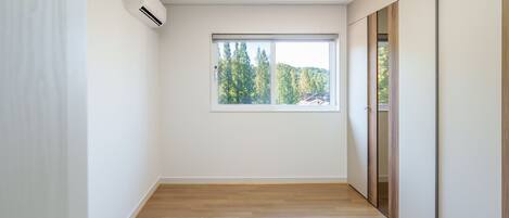 A room with a large window, wooden flooring, and a sliding door.