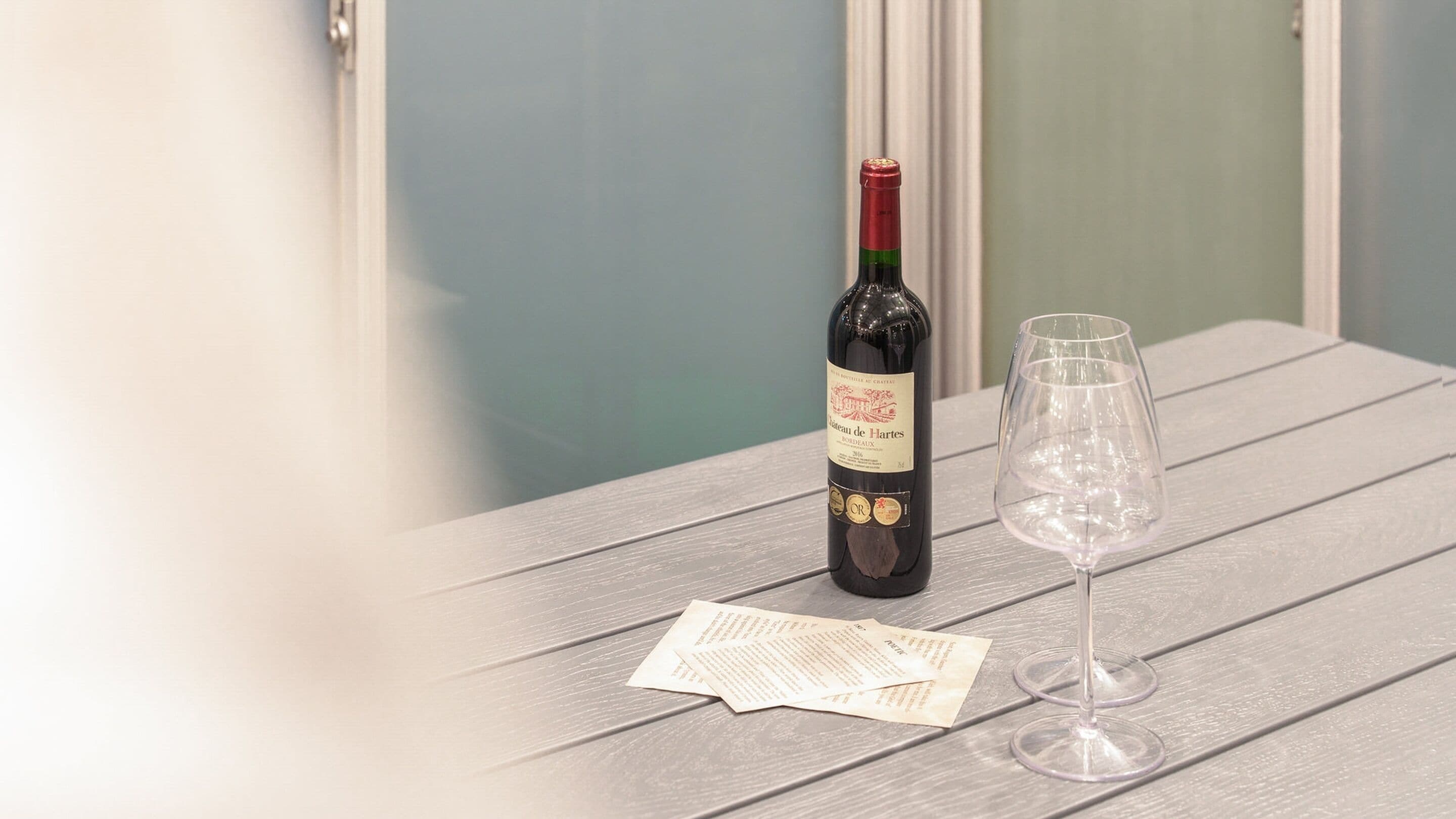 A bottle of Chateau de Larres wine and an empty wine glass on a wooden table with a menu.