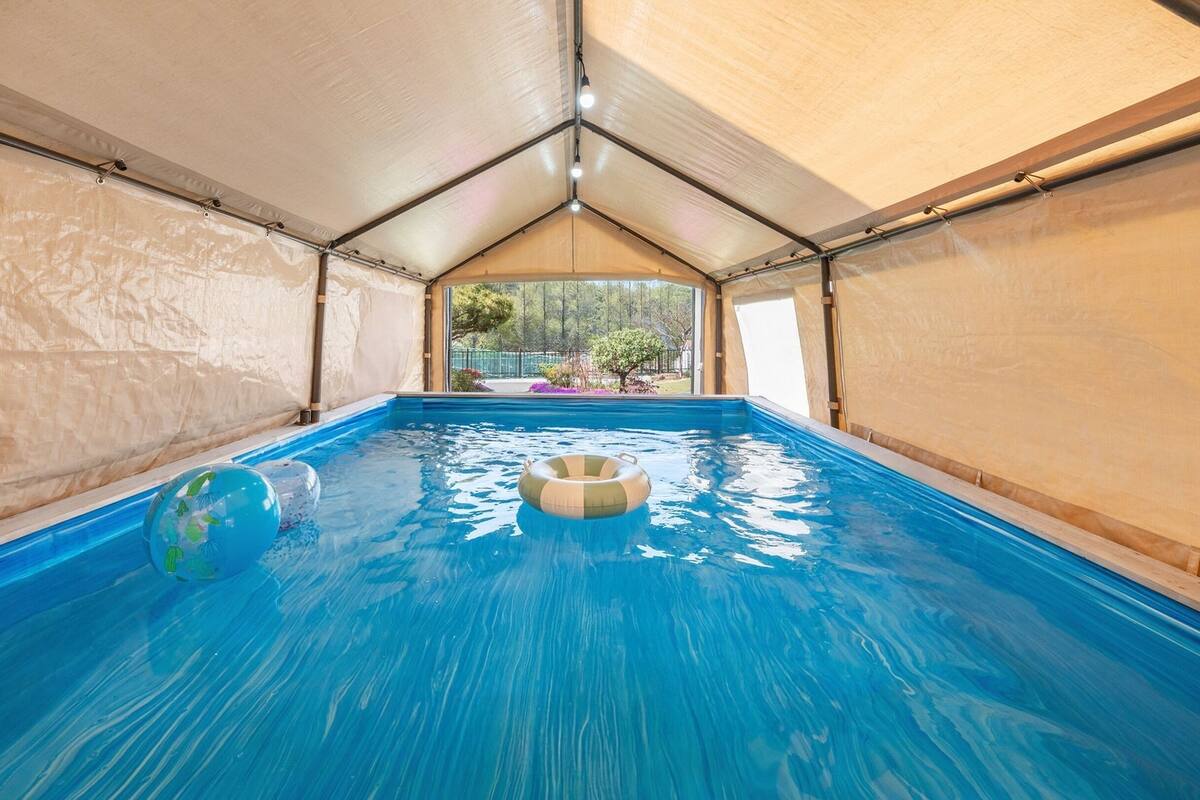 An indoor swimming pool with clear blue water, surrounded by beige walls and a peaked roof structure.