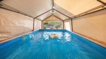 An indoor swimming pool with clear blue water, surrounded by beige walls and a peaked roof structure.