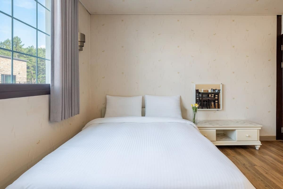 A bedroom with a large bed, a bedside table, a mirror, and a window.