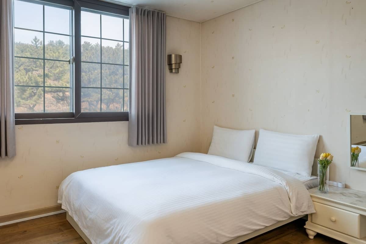 A bedroom with a bed, a nightstand, a mirror, and a window with curtains.