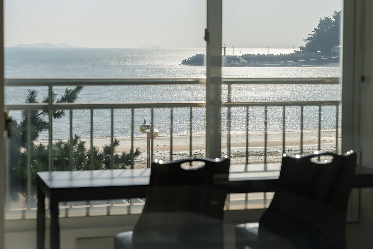 A balcony with a view of the sea, a table, and chairs.