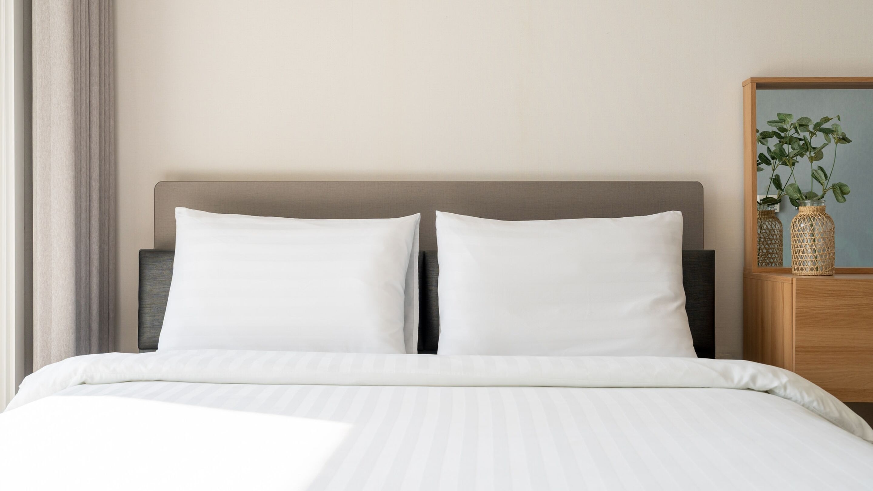 A neatly made bed with white linens and a grey headboard.