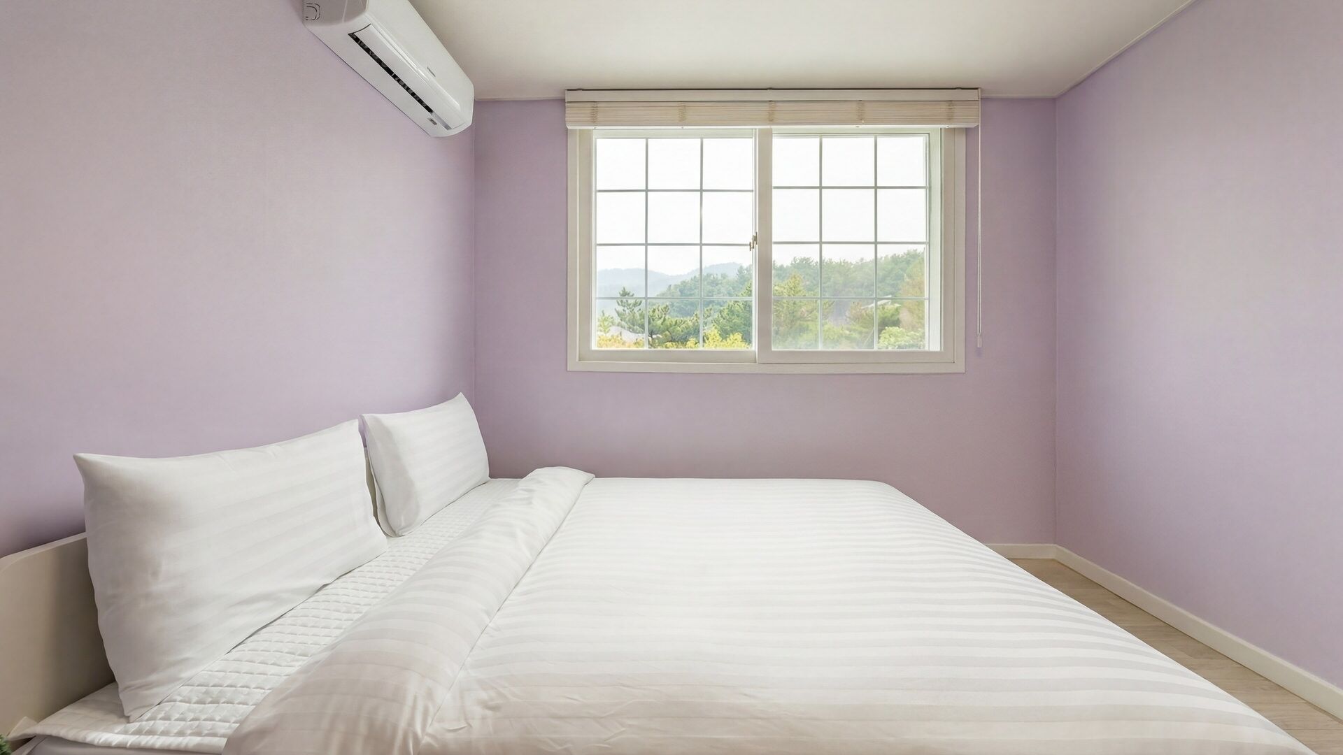A bedroom with a bed, a window with a view, and an air conditioning unit.