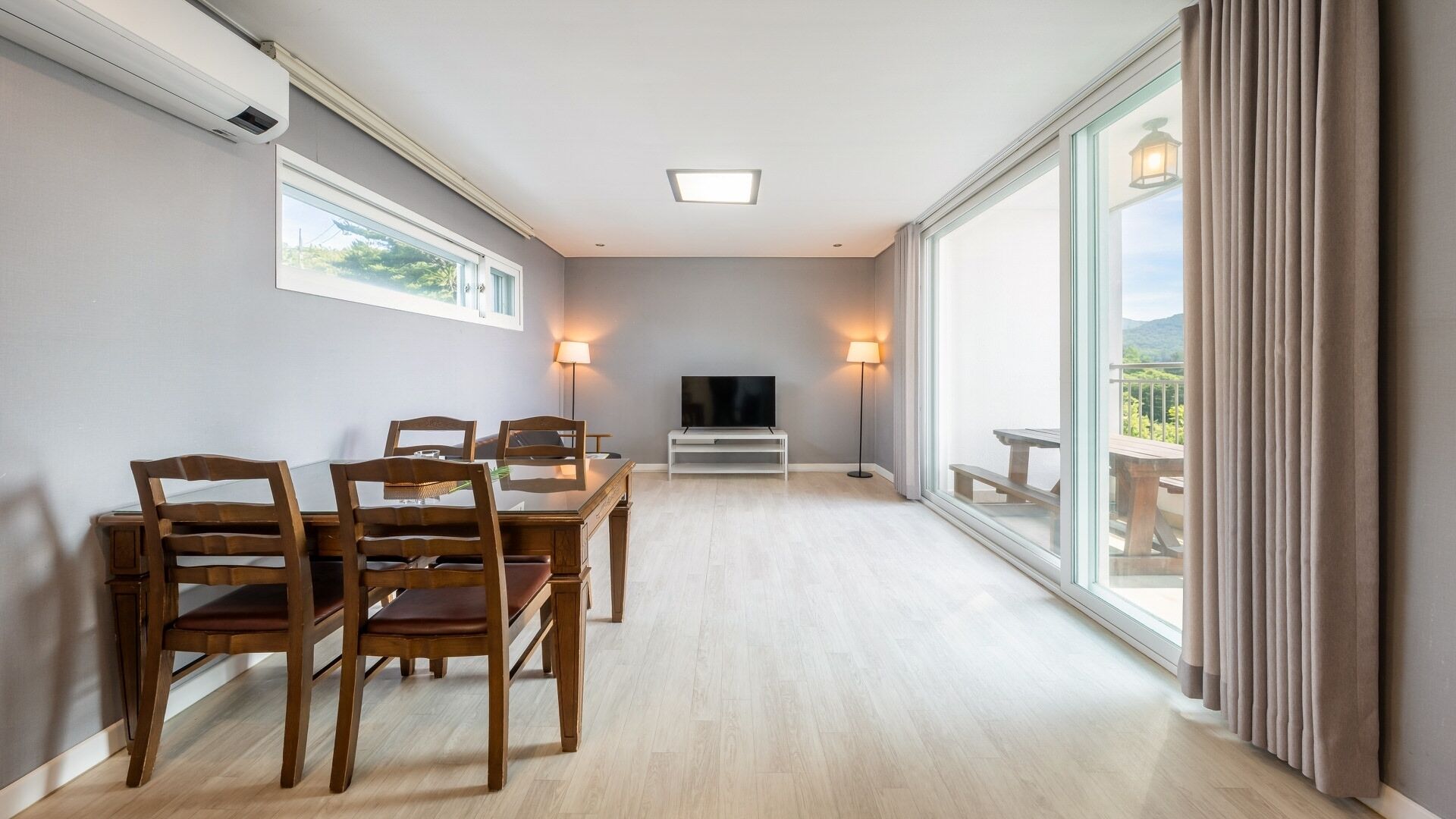 A spacious room with a dining table, chairs, a TV, and a large window with a view.