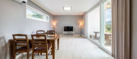 A spacious room with a dining table, chairs, a TV, and a large window with a view.