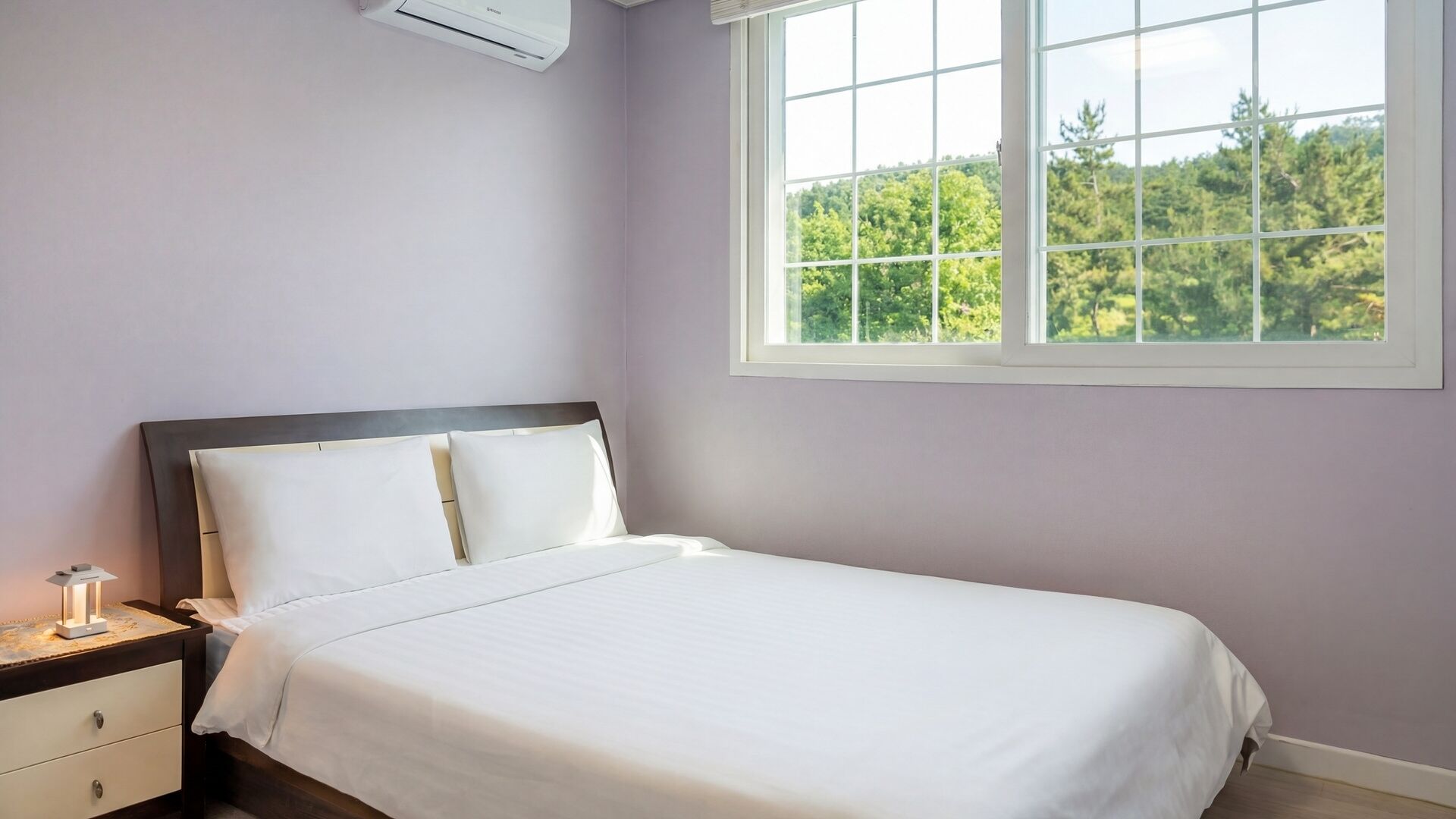 A bedroom with a bed, nightstand, lamp, and a window with a view of trees.