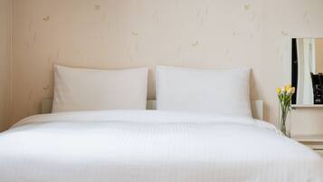 A neatly made bed with white linens, a wall with a subtle pattern, and a vase with flowers on a nightstand.
