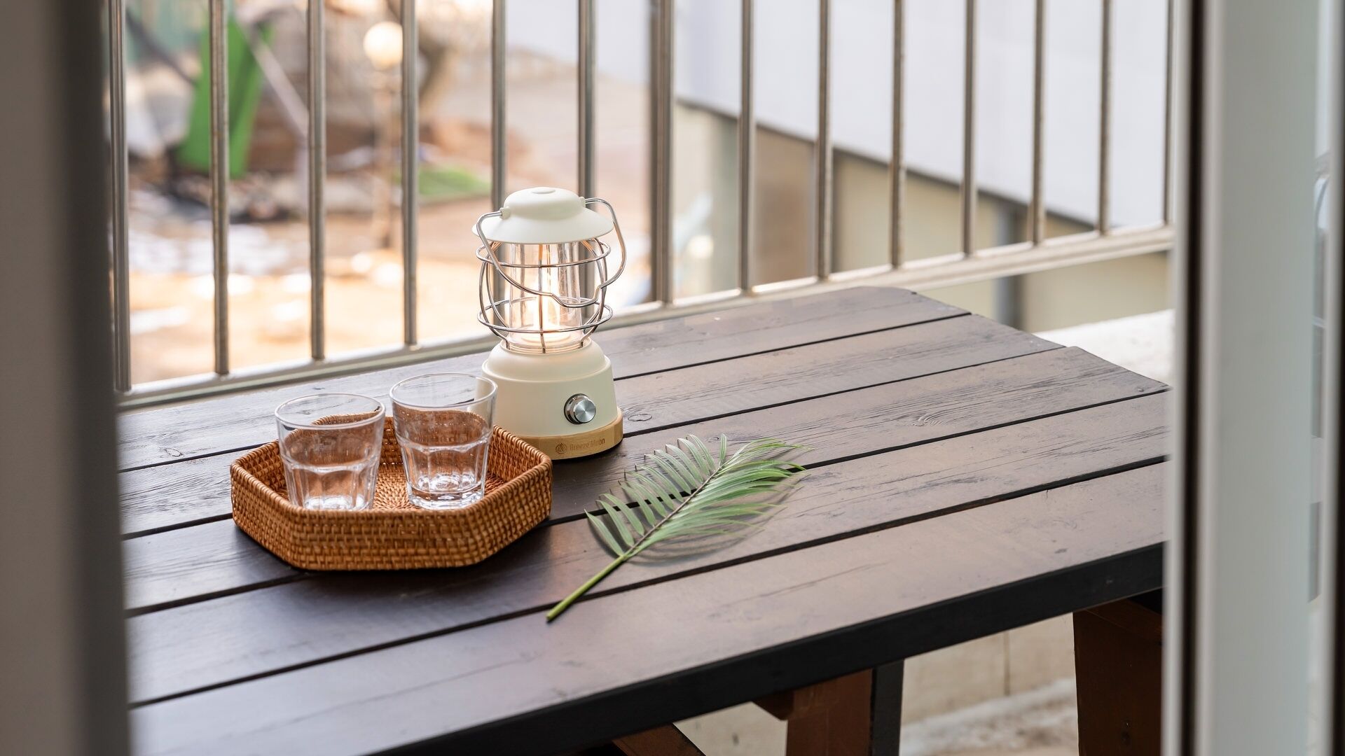 A wooden table with a portable blender, two glasses, and a leaf.