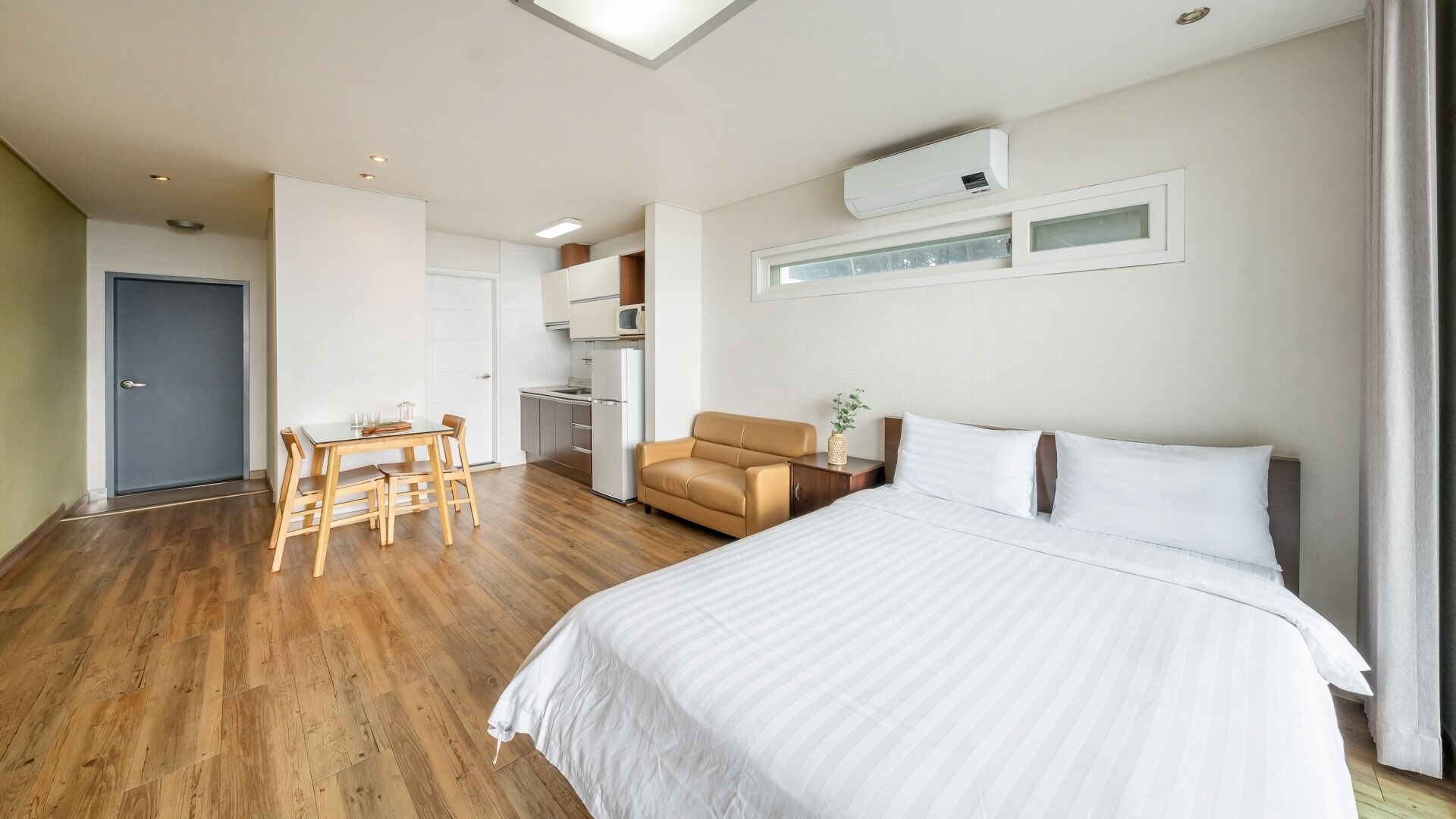 Habitación de hotel con cama, escritorio, silla, kitchenette y baño.