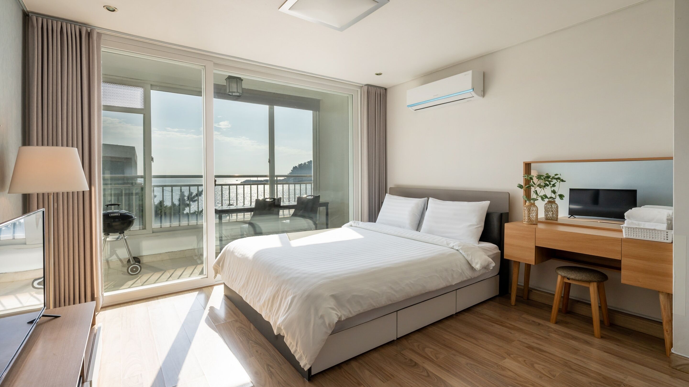 Ein Hotelzimmer mit Bett, Schreibtisch, Fernseher und Balkon mit Meerblick, sowie einer Schiebeglasdoor.