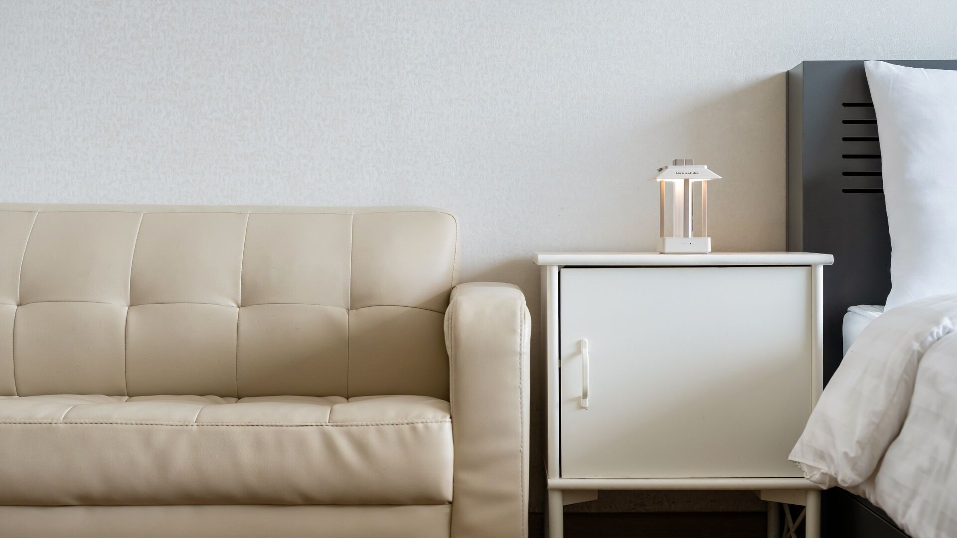 Ein sofas in neutralen Farben, ein Nachttisch in Weiß mit einer Lampe und ein Bett mit einem weißen Kissen.