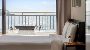 Habitación de hotel con cama, mesita de noche, mesa y sillas, y balcón con vistas.