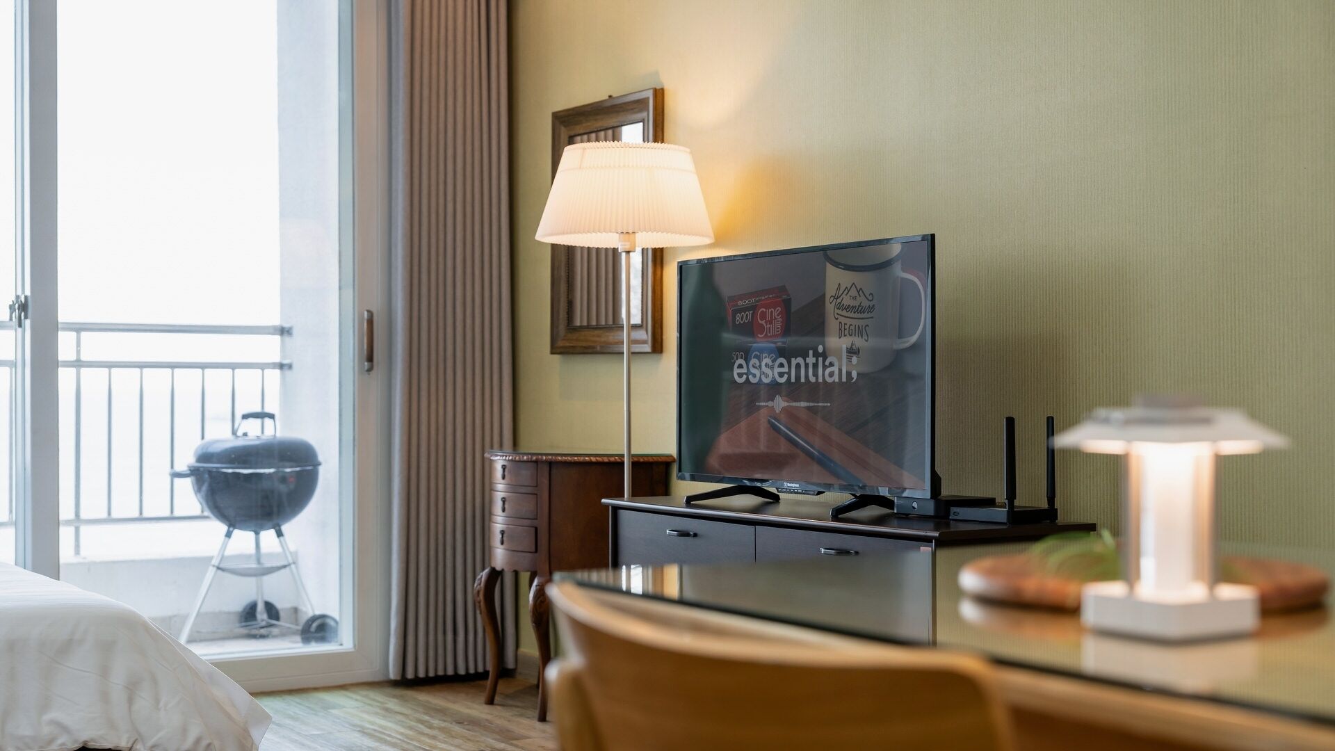 Une chambre d’hôtel avec une télévision, une lampe, un barbecue à l’extérieur de la fenêtre et un lit.