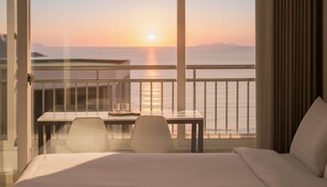 Habitación de hotel con balcón y vista al mar al atardecer.
