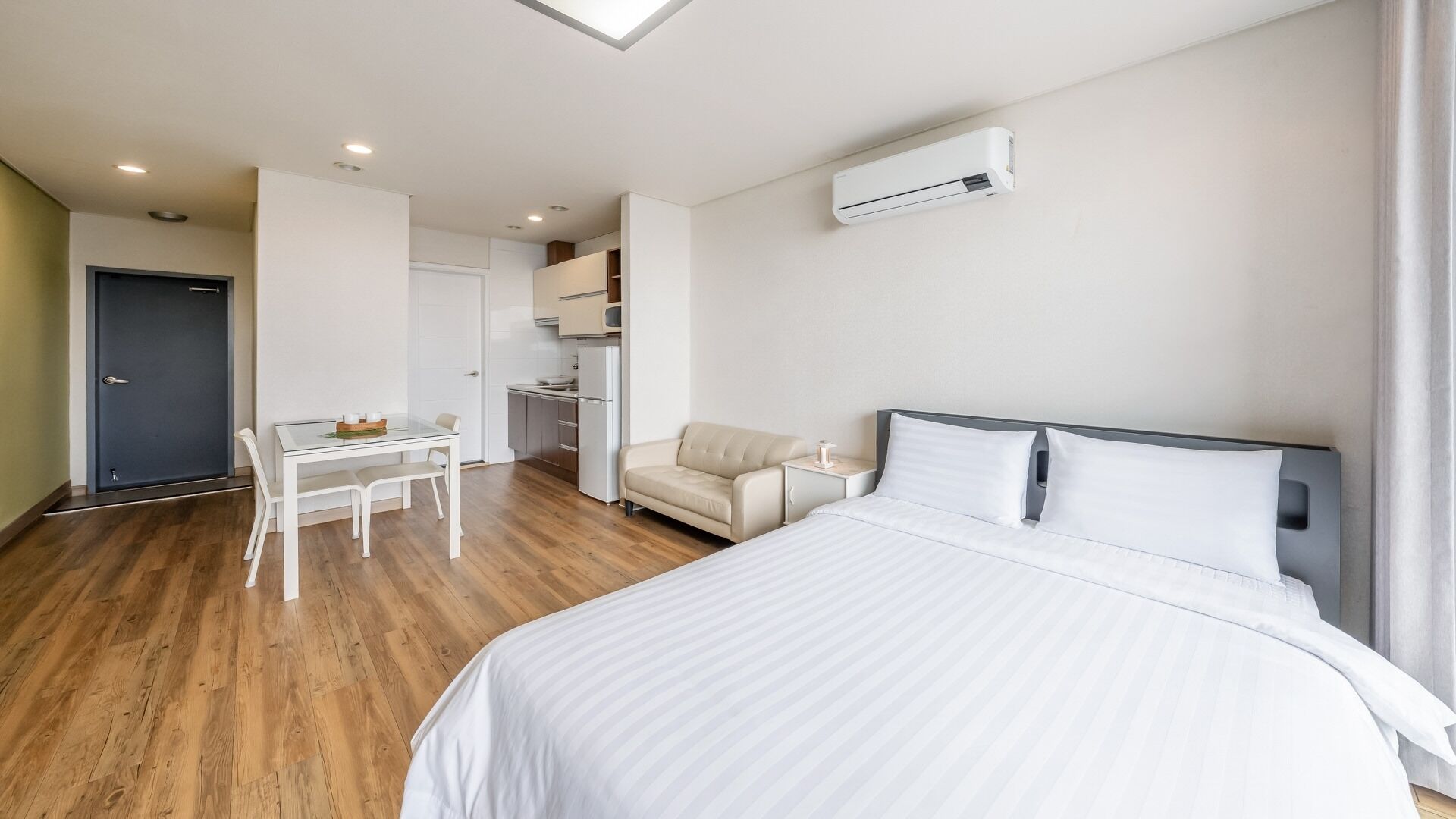 Habitación de hotel con cama, una mesita, una silla, kitchenette y aire acondicionado.