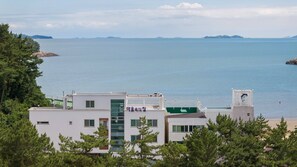 Um edifício costeiro com uma placa em idioma estrangeiro, rodeado por árvores e com vista para o mar.