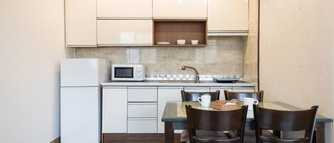 Cocina compacta con refrigerador, microondas y lavamanos. Hay una mesa de comedor con sillas y una cesta.