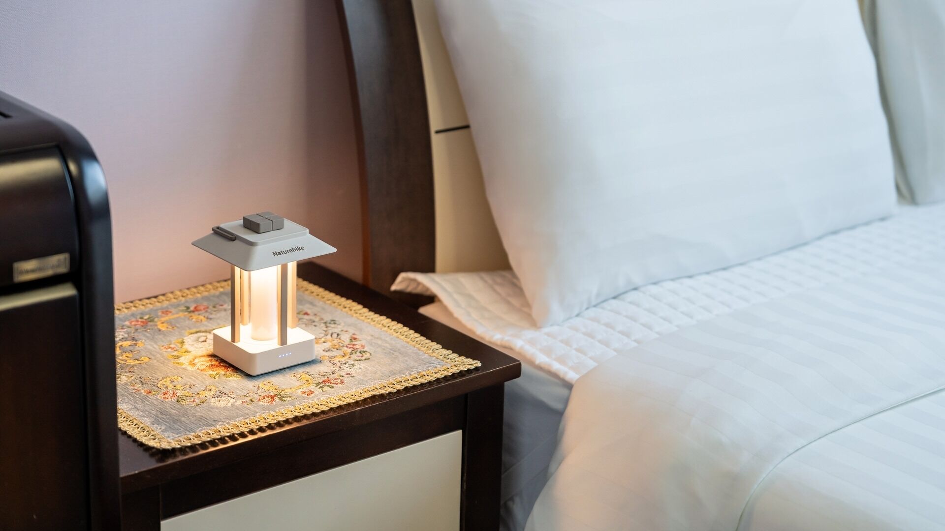Ein Hotelzimmer mit Nachttisch, Lampe, Bett und einem dekorativen Teppich.