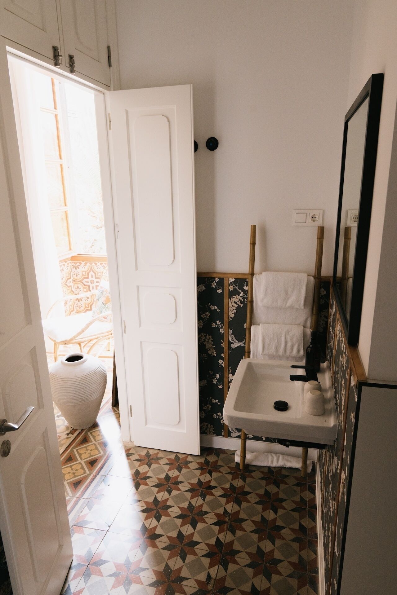 Un baño con lavamanos blanco, un espejo y una puerta que da a un balcón.