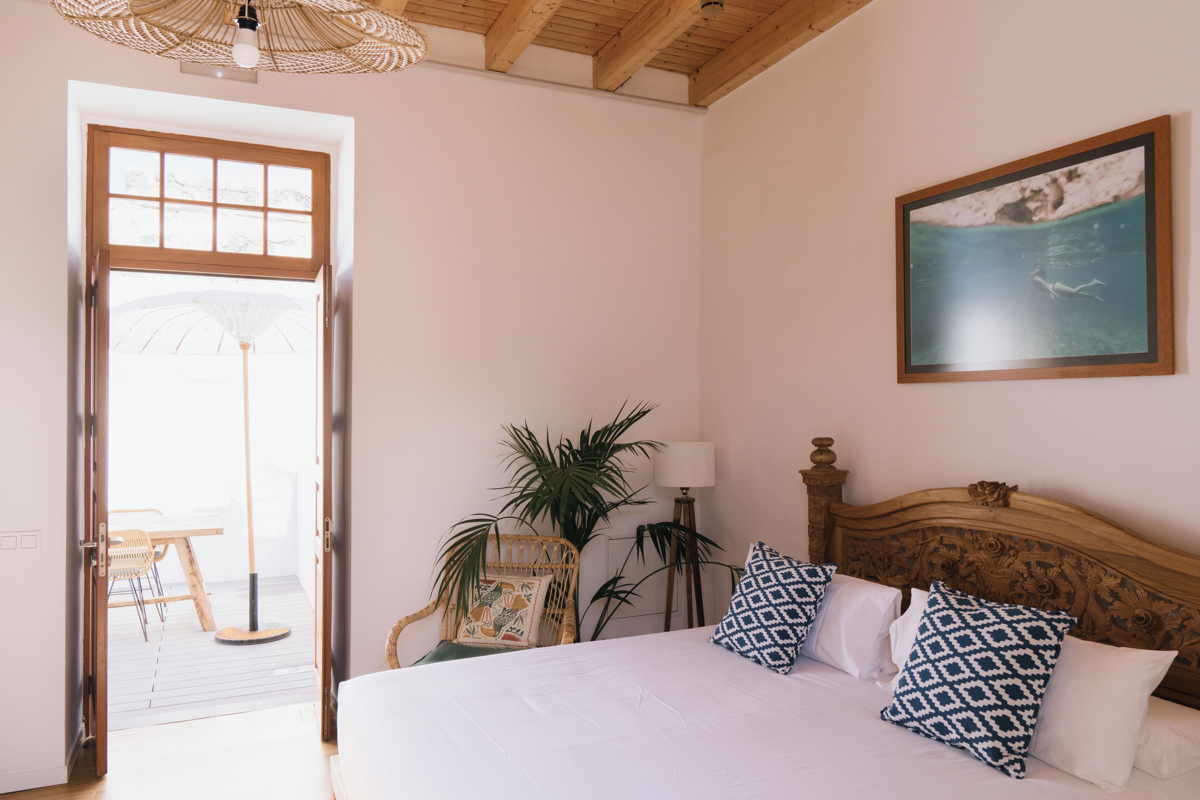 A bedroom with a wooden headboard, a bed with patterned pillows, a standing lamp, and a framed picture on the wall.