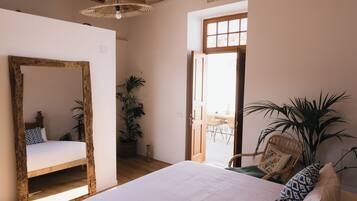 A bedroom with a large bed, a wooden-framed mirror, a potted plant, and a wicker chair.