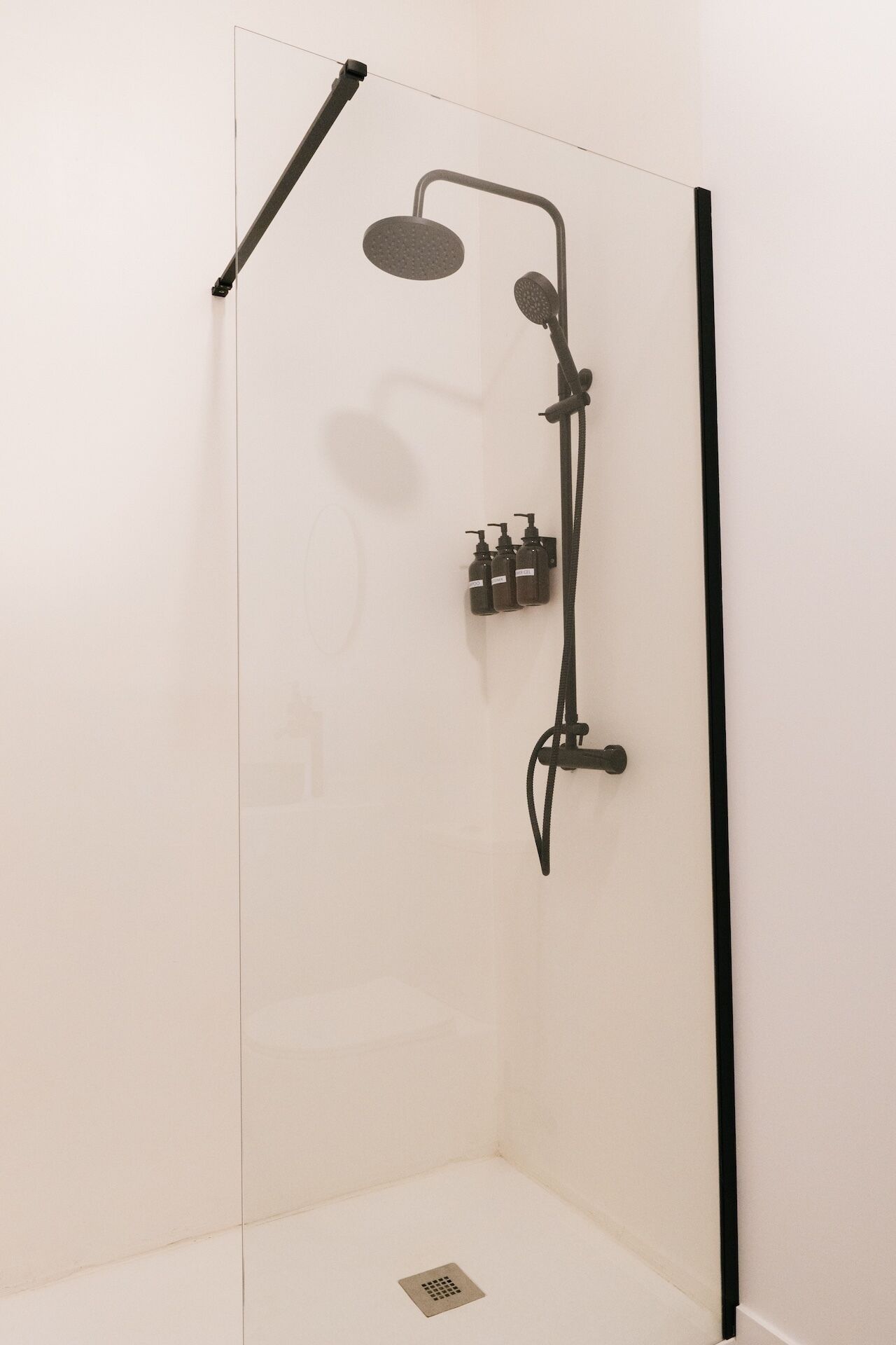 A modern shower enclosure with a glass door, a handheld showerhead, a wall-mounted faucet, and a handheld showerhead.