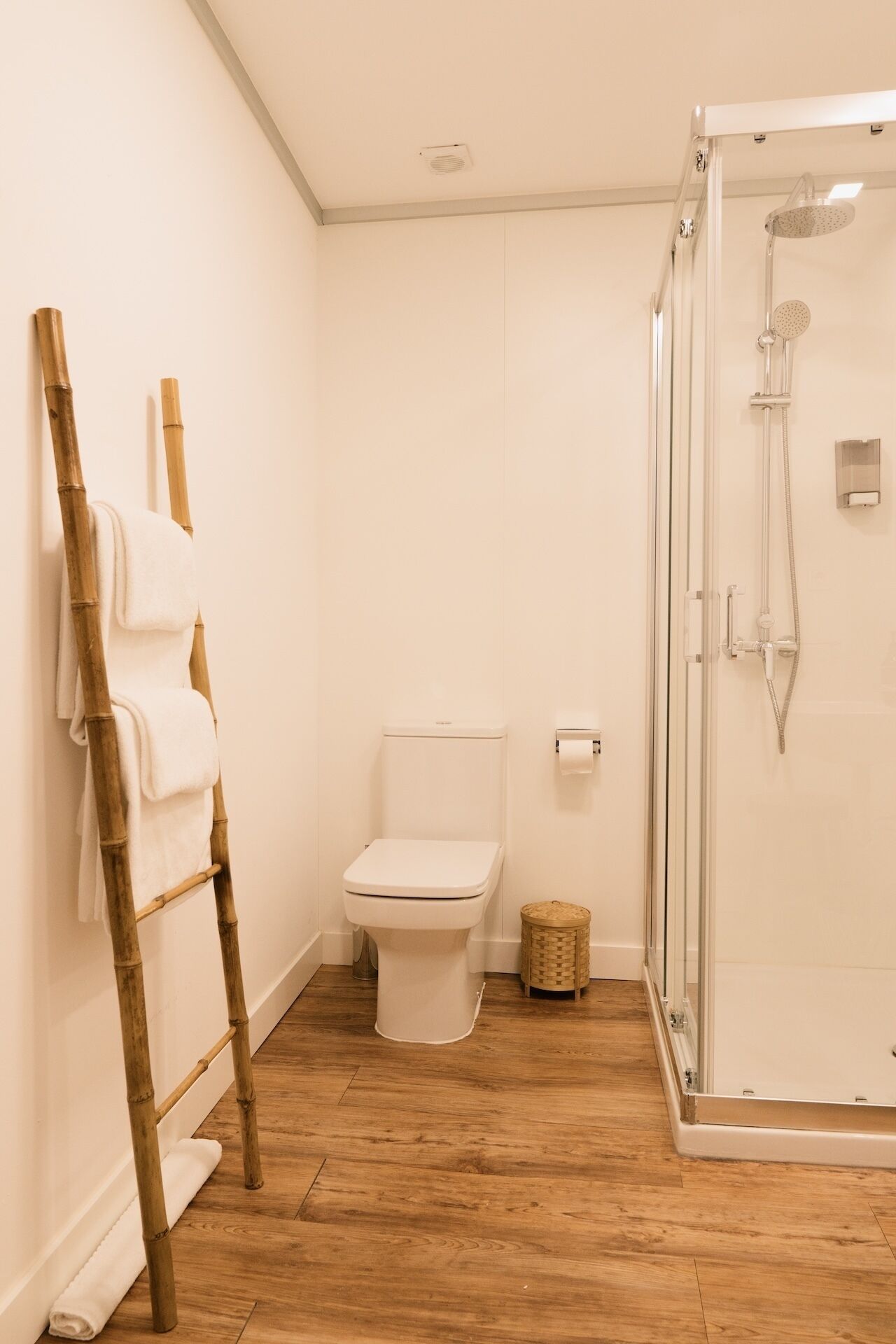 A bathroom with a toilet, a shower, and a bamboo towel rack.