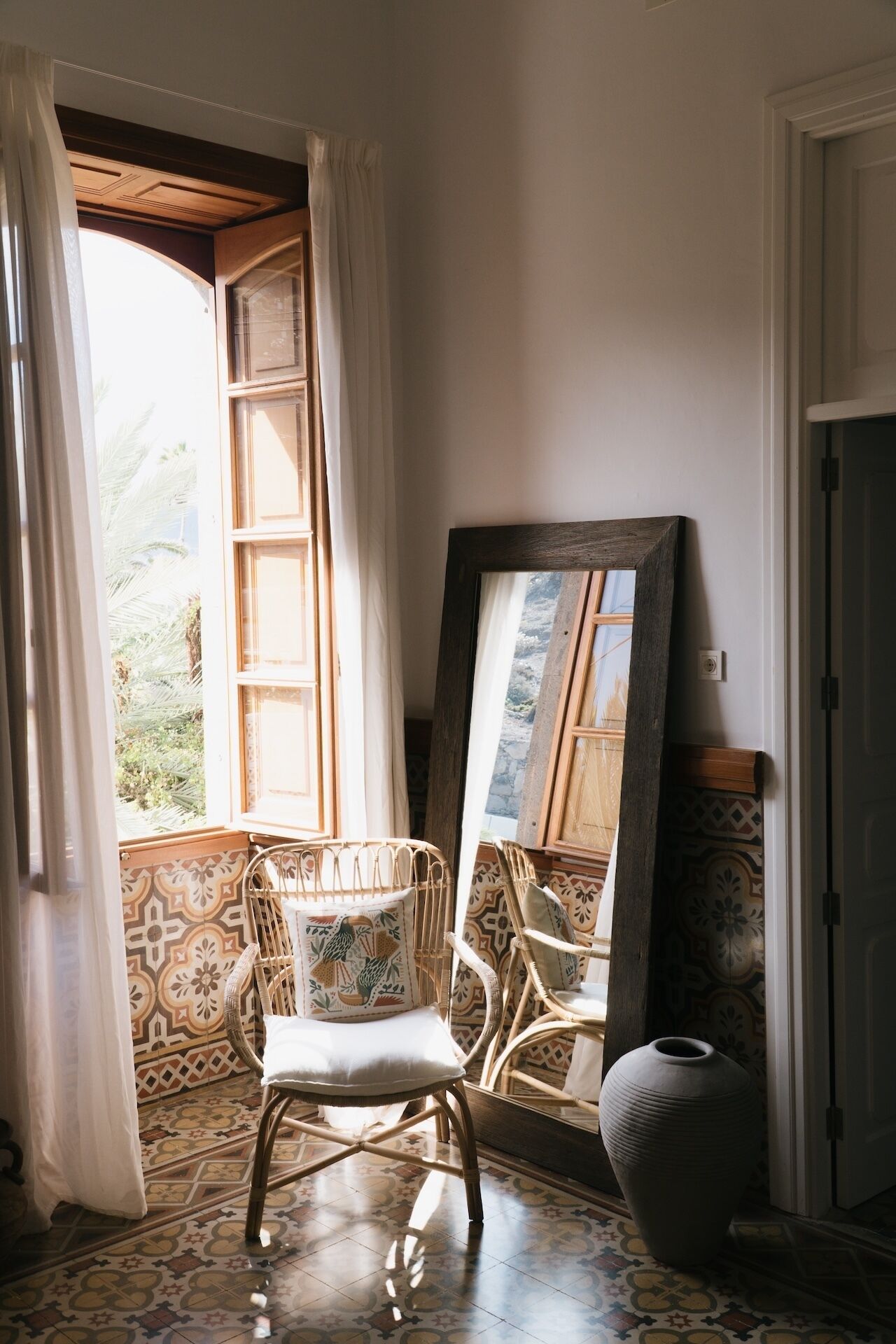 A room with a wicker chair, a large mirror, and patterned tiles.