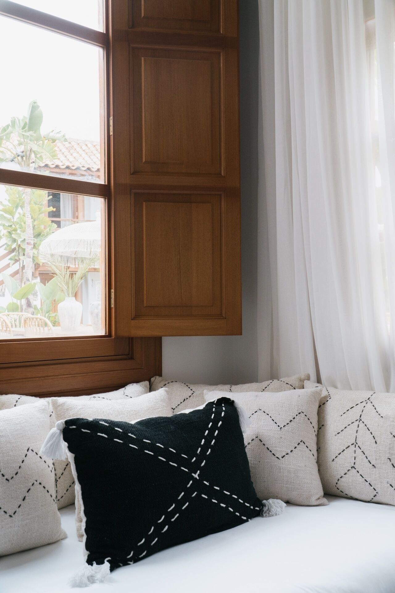 A window seat with a wooden cabinet above and white curtains to the right.