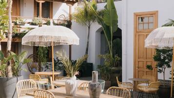 An outdoor patio with wicker furniture, white umbrellas, and potted plants.