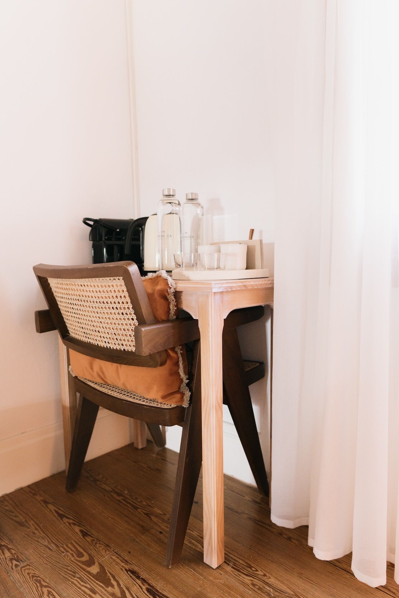 A small wooden table with a chair, a coffee maker, and various bottles and containers on it.