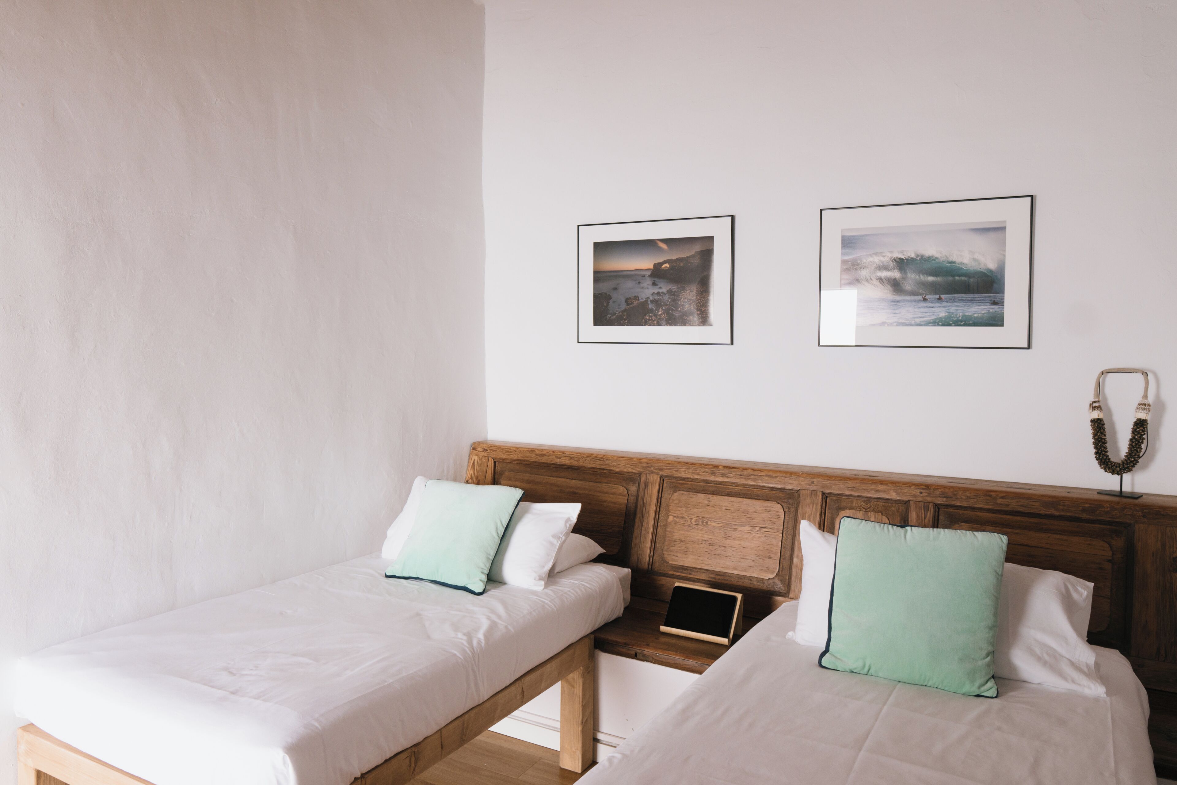 A bedroom with two single beds, a wooden headboard, and two framed pictures on the wall.