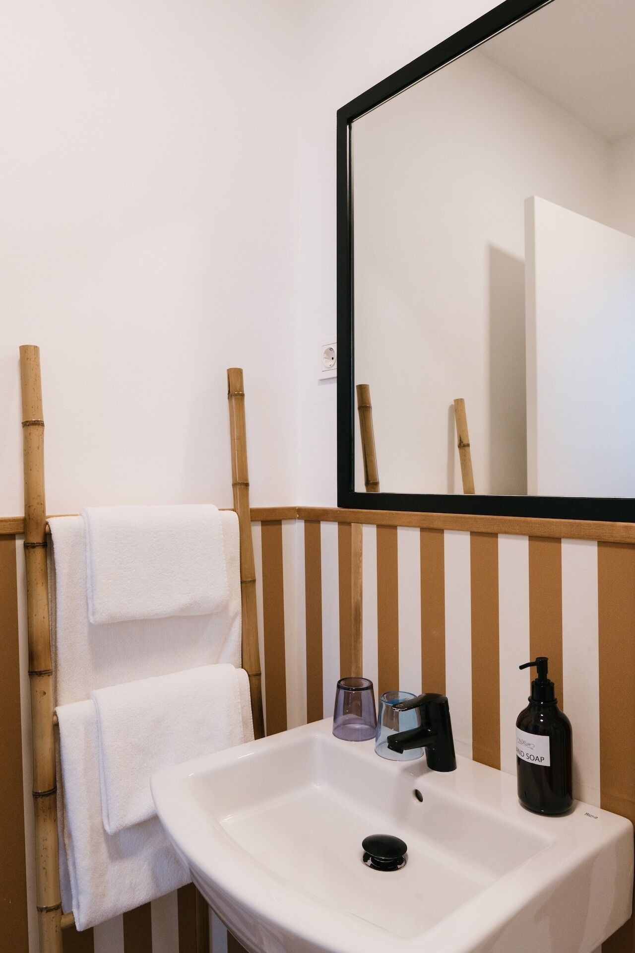 Een badkamer met een witte wastafel, een spiegel en twee handdoeken aan een bamboe rek.