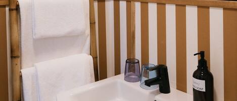 Un baño con un lavamanos blanco, un espejo y dos toallas colgadas en un soporte de bambú.