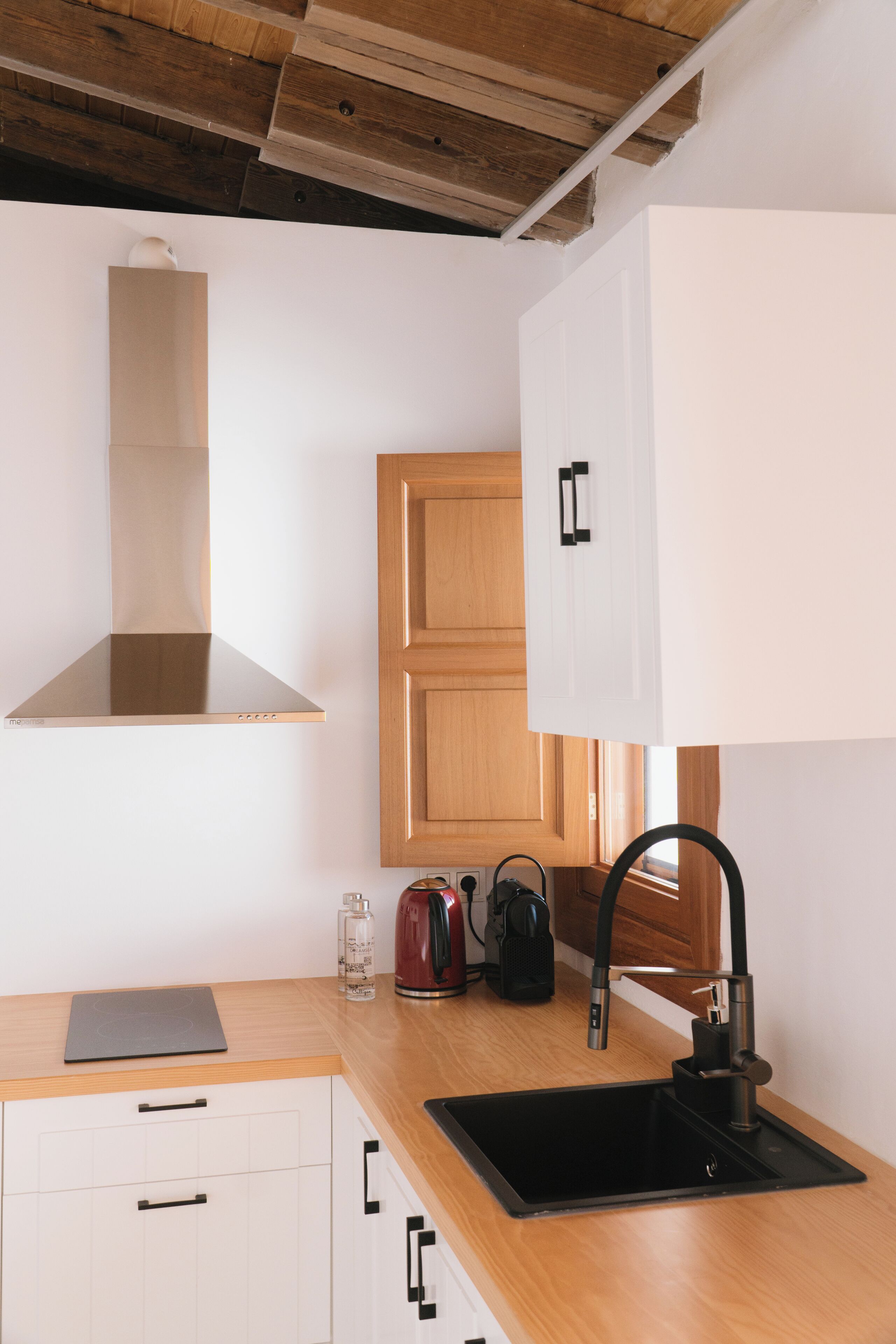 Une cuisine moderne avec des meubles en bois, une hotte en acier inoxydable, un évier noir et une bouilloire posée sur le plan de travail.
