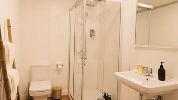 Un baño con inodoro, ducha con mampara de vidrio y lavamanos con artículos de aseo.