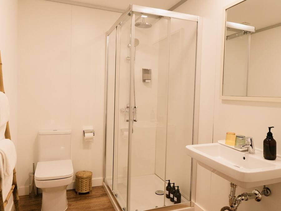 Un baño con inodoro, ducha con mampara de vidrio y lavamanos con artículos de aseo.