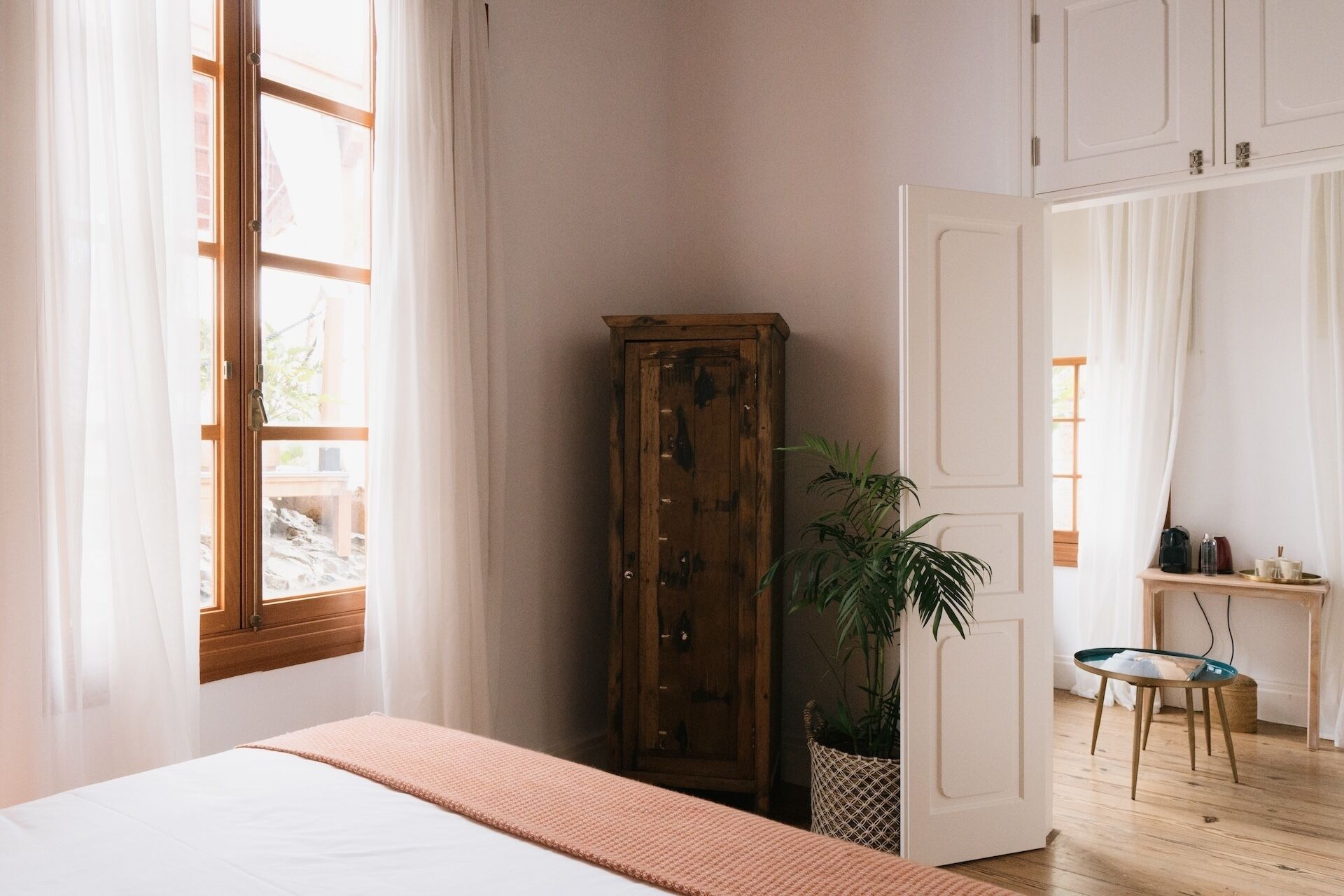 Een slaapkamer met een bed, een houten garderobe, een bloempot en een bureau met een stoel.