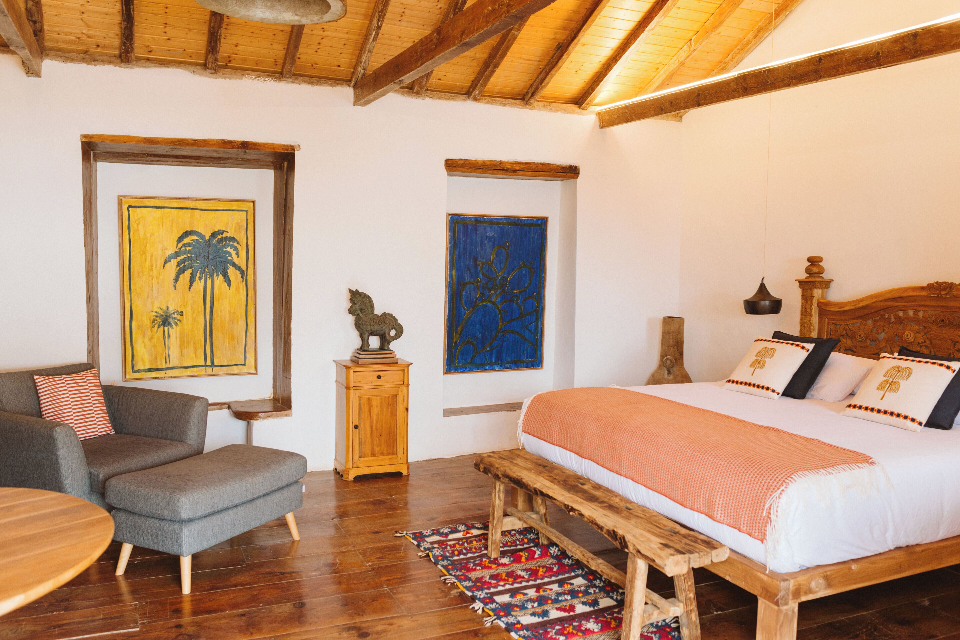 Un dormitorio con una cama de madera, un banco, una mesita y dos sillas.